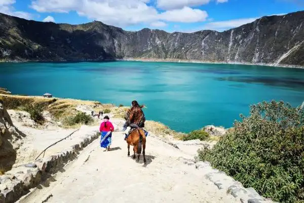 Turistas bajan a caballo hacia la laguna turquesa del cráter de Quilotoa