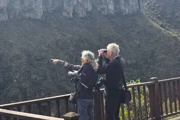 Visitors on a mountain viewpoint deck spotting condors with binoculars and a spotting scope