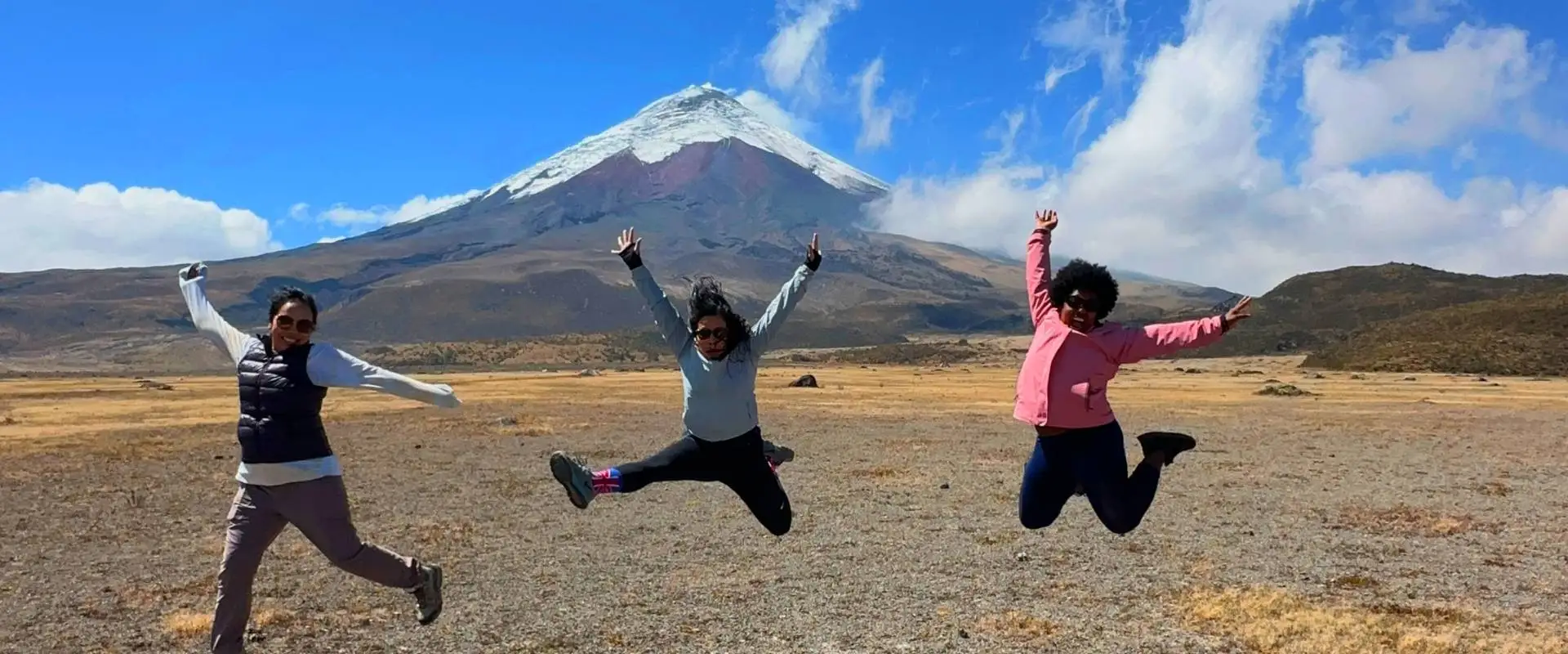 Tres viajeras saltando en el páramo frente al volcán Cotopaxi