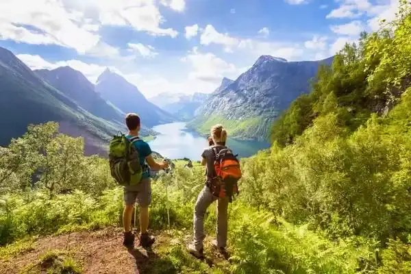 Hikers resting at a scenic overlook above a turquoise lake surrounded by green hills