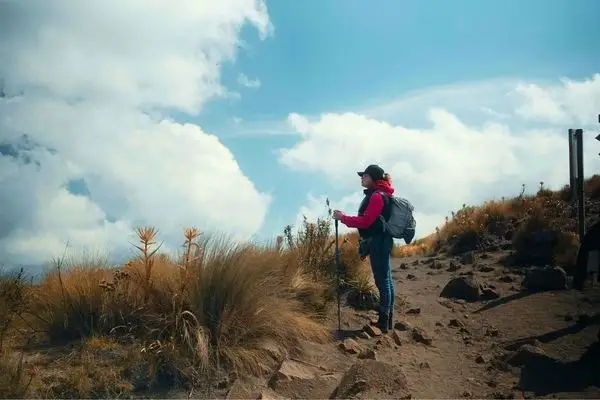 Hiker with trekking poles pausing on a highland trail with clouds in the background