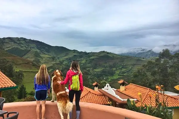 Two hikers and a dog admire the Andean valley from an Isinlivi lodge terrace