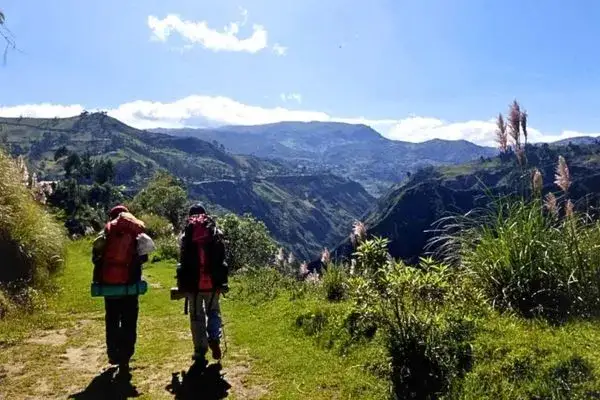 Hikers walking a green mountain trail toward the Sigchos valley
