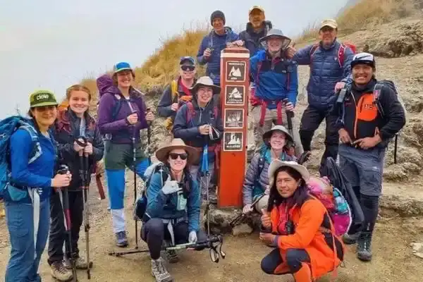 Hiking group posing at a trail marker on a misty Andean mountain trail
