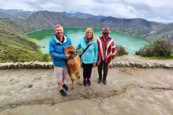 Tourists posing with a local guide and alpaca above Quilotoa's crater lake
