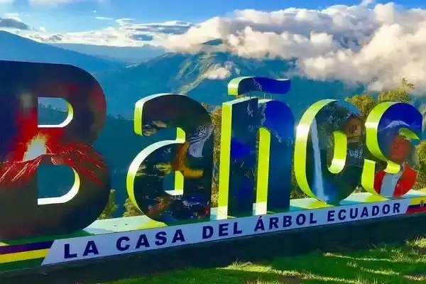 Banos sign at the Casa del Arbol lookout with the Andes mountains behind it