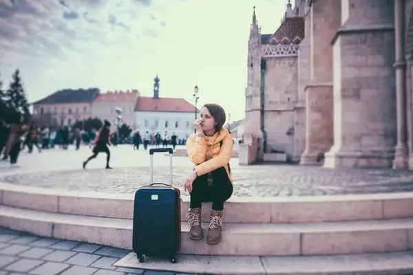 Traveler with a suitcase resting on a colonial plaza staircase during a stopover