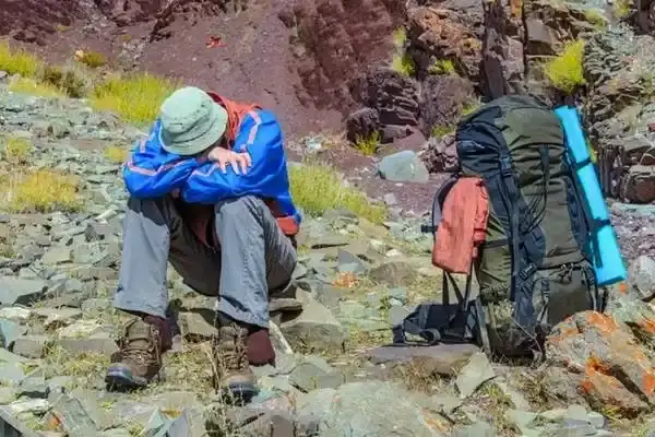 Tired hiker resting beside a backpack on a rocky volcanic slope near Papallacta