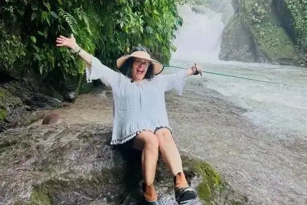 Woman celebrating beside a rushing waterfall in Mindo cloud forest