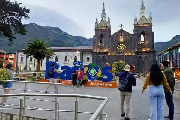 Tourists at the colorful Banos sign in front of the basilica at dusk