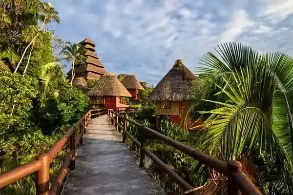 Wooden walkway connecting thatched-roof cabins at a luxury Amazon lodge