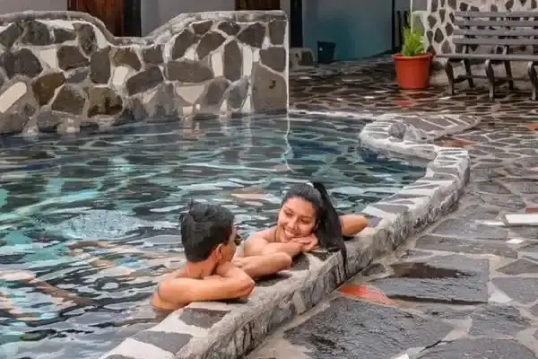 Couple resting at the stone edge of a thermal pool on a rainy afternoon
