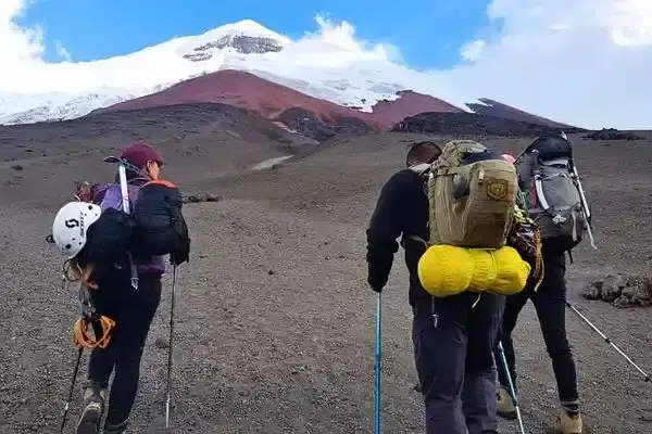 Group of trekkers with backpacks and hiking poles walking toward Cotopaxi volcano