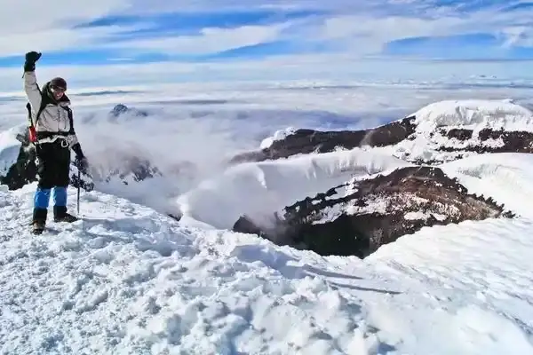 Climber raising an arm at Cotopaxi's summit crater rim above the clouds