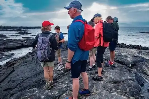Hikers walking the coastal lava trail near Tintoreras at sunset