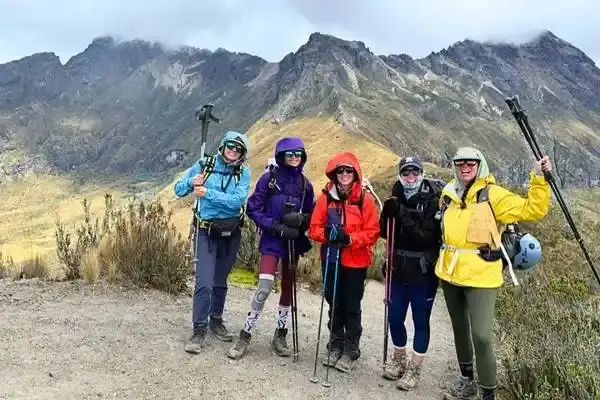 Five hikers with trekking poles and backpacks posing on a mountain ridge trail