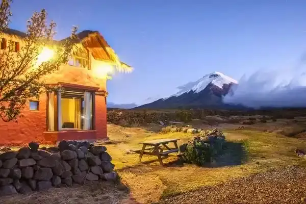 Tambopaxi lodge lit up at dusk with Cotopaxi volcano in the background