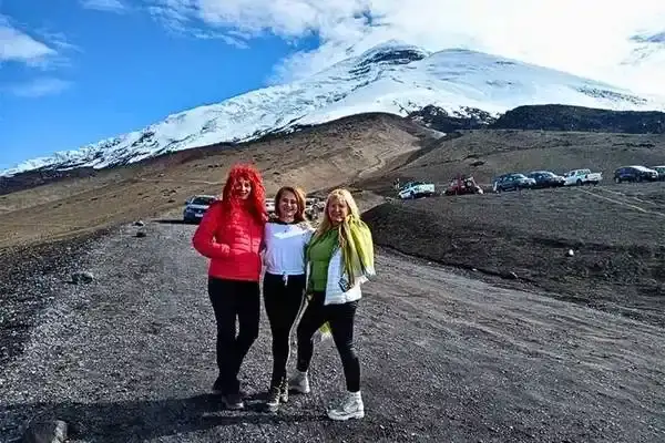 Three visitors near Cotopaxi volcano with tour vehicles parked in the distance