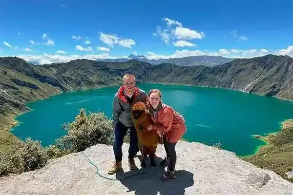 Couple with a llama posing above the turquoise waters of Quilotoa crater lake