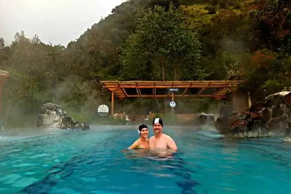 Couple smiling in a warm thermal pool at Papallacta hot springs with misty mountains behind