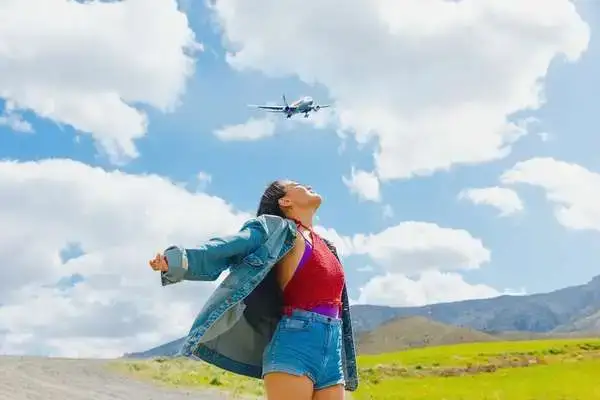 Traveler with arms outstretched under a clear Andean sky as a plane flies over, the best time to visit Ecuador