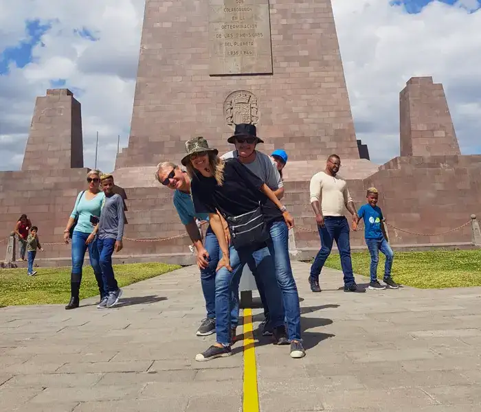 Turistas posando sobre la línea ecuatorial frente al Monumento Mitad del Mundo