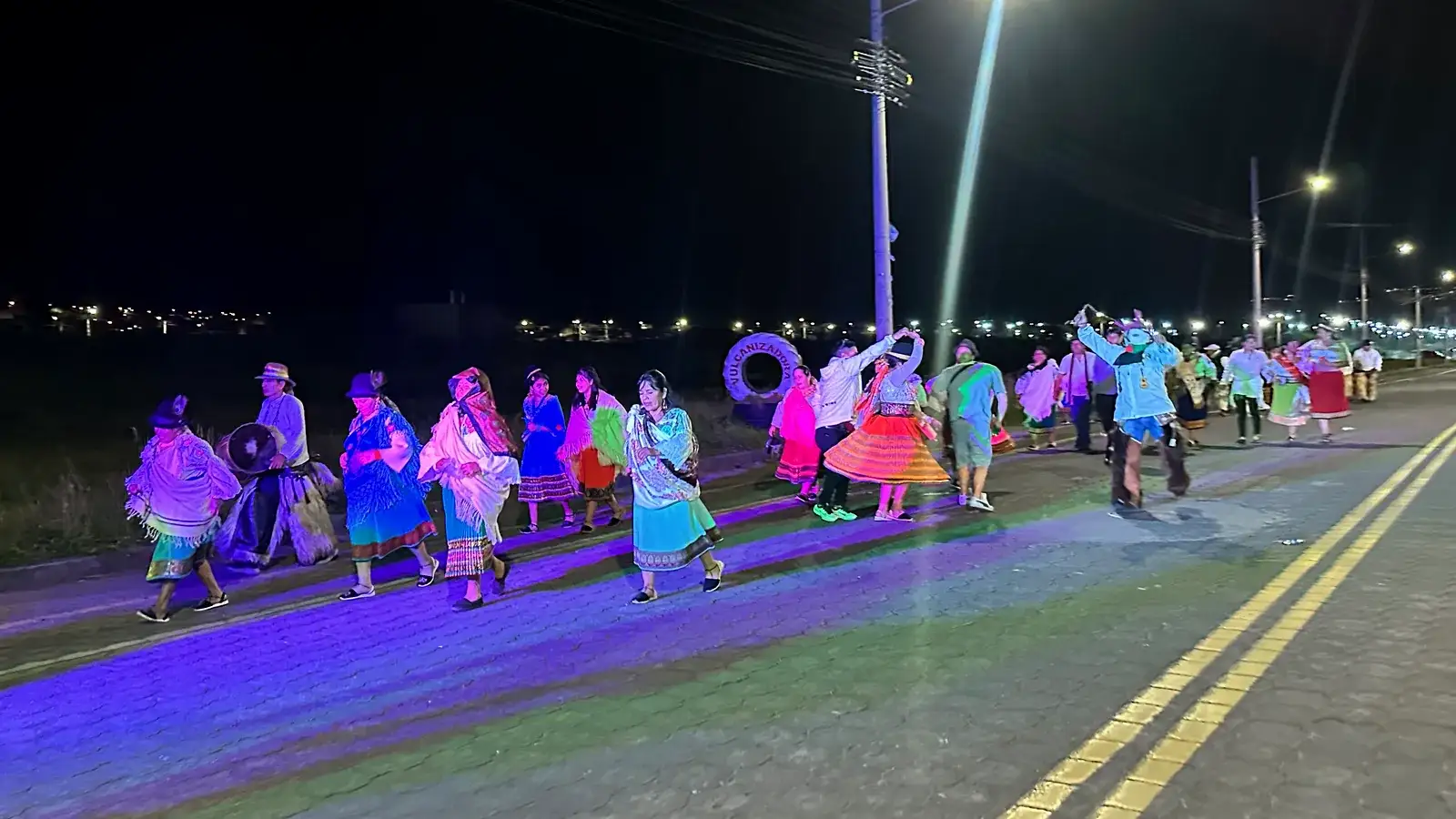 Dancers in embroidered blouses and wide skirts parading at night during the San Pedro festival in Cayambe