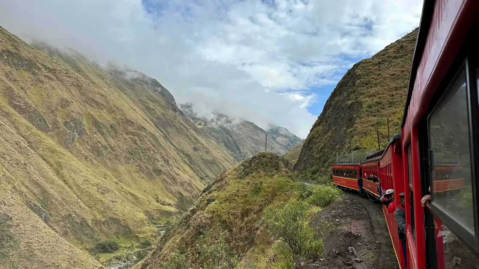 Red train cars of the Devil's Nose railway hugging a cliff above a deep Andean canyon near Alausí